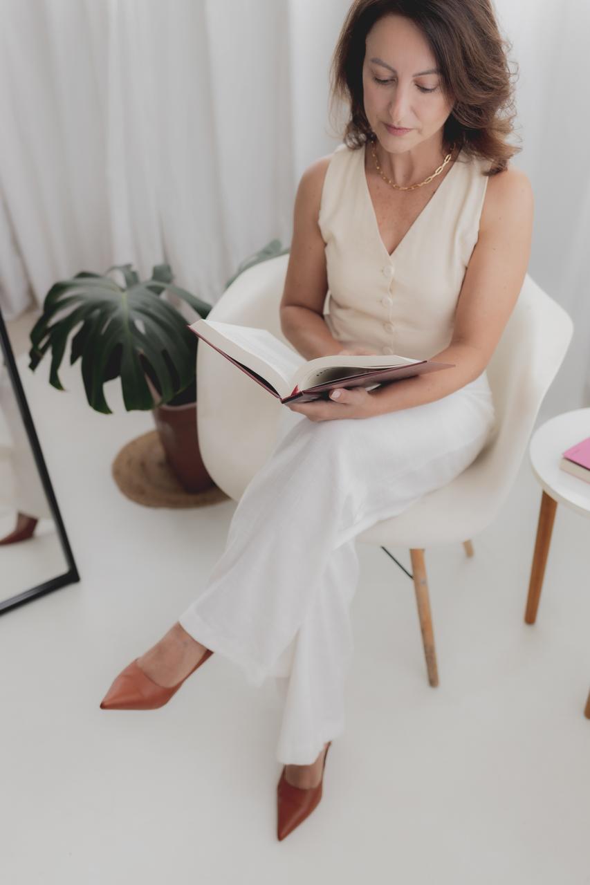 Vanessa Helena sentada em um ambiente claro, com um livro